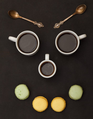 Tree cups coffee and macaroon arranged in happy face, on blackの写真素材