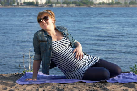 Pregnant woman sitting on the river coast.の写真素材