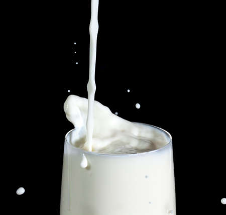 Pouring Milk in Glass, on black backgroundの写真素材