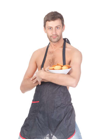 Attractive man trying his hand at baking wearing an apron and carrying a bowl of freshly baked cookies isolated on whiteの写真素材