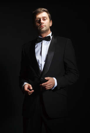 Dramatic portrait of a suave handsome man in a tuxedo and bowtie highlighted in darknessの写真素材