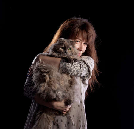 Young beautiful smiling woman holds fluffy cat, on black backgroundの写真素材