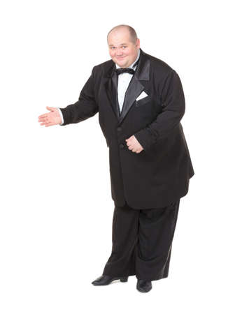 Elegant fat man in a dinner jacket and bow tie smiling charmingly as he holds out his hand to the side gesturing in that directionの写真素材