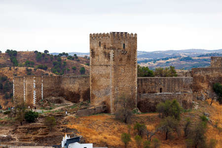 Fortified stone lookout tower with crenellations alongside a perimeter wall affording a view over the surrounding countryside and valleyの写真素材