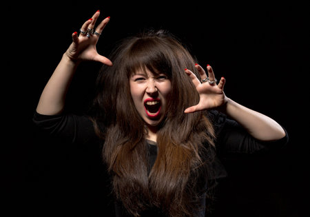 Woman throwing a temper tantrum screaming in anger and clawing the air with her hands on a dark...