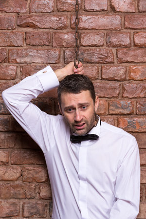 Conceptual image of a desperate handsome businessman in a bow tie standing against a brick wall with...