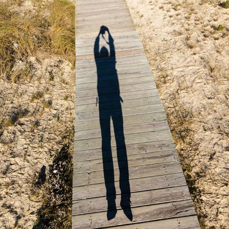 Elongated Shadow Jumping Man on a Wooden Walkway, sunny dayの写真素材