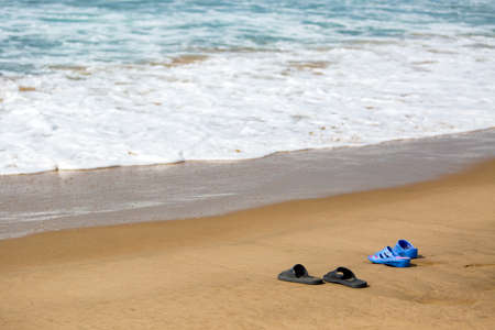 Women's and Men's Slippers on a Sandy Ocean Beach, summer vacation conceptの写真素材