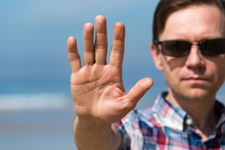 Man in Sunglasses Showing Stop Sign with his Hand, blue sky backgroundの写真素材