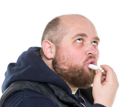Bald Bearded Fat Man Uses a Protective Lipstick, on white backgroundの写真素材