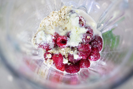 Food in a blender, close-up. Strawberries, raspberries, oats, protein, milk.