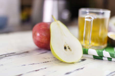 Close-up. A neatly cut half of a juicy ripe pear. Lies next to a whole red pear and a cup of tea on a wooden vintage table.の写真素材