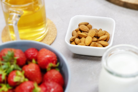 Almond in a bowl on the table next to fresh milk, strawberries and warm herbal tea. Morning in the...