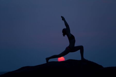 Warrior pose from yoga by woman silhouette with the first light of rising sunの写真素材