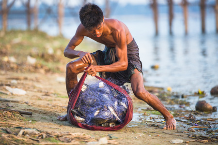 MANDALAY, MYANMAR - JANUARY 9, 2015 : Fisherman near U Bein bridge in Myanmar pack a net full of fish.のeditorial素材