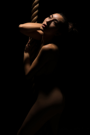 Beautiful young nude Asian woman clinging to a climbing ropeの写真素材