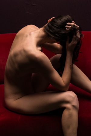 Pretty young brunette nude on a red couchの写真素材