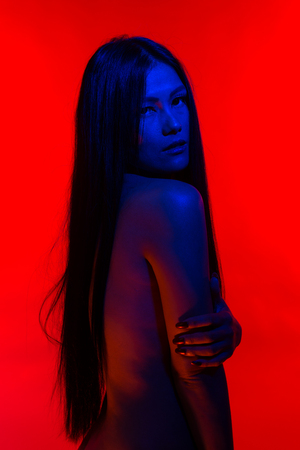 Beautiful petite Filipino woman lit in blue and redの写真素材