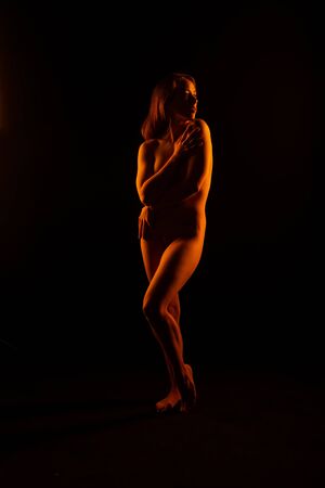 Petite young brunette standing nude in orange lightの写真素材