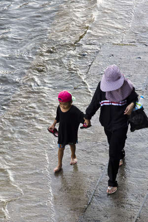 Bangkok - November 2011: Thai lady and her son walking in the flood road. on 7 November 2011at Ramintra Soi 14 road, Ladprao, Bangkok, Thailand. The boy look happy to see the flood. It is the first time for him to see alot of water.のeditorial素材