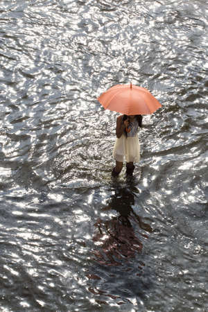 Bangkok Thailand 8 November 2011: A working women hold an umbrella to protect the heat from the sun, ware a long rubber boots, walking across the road to buy goods from convenience stores.の写真素材