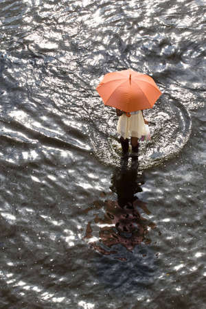 Bangkok Thailand 8 November 2011: A working women hold an umbrella to protect the heat from the sun, ware a long rubber boots, walking across the road to buy goods from convenience stores.の写真素材