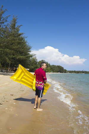 The  European man walking and carrying a yellow rubber mattress at the beach at Koh Mak island, Trat, Thailandの写真素材