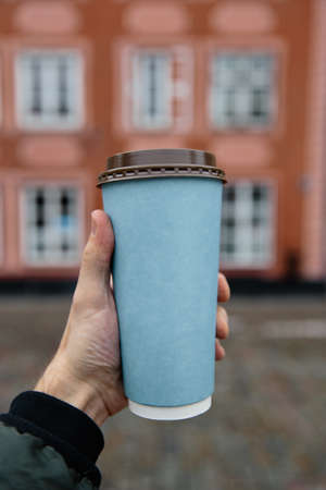 Mockup ad: Male hand holding a blank paper cup in an old town backgroundの写真素材