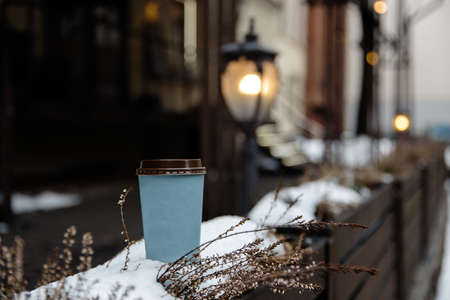 Mockup ad: a blank paper cup standing on a fence in an old town backgroundの写真素材