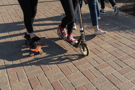Young people in jeans and sneakers skating and using a scooter on a concrete brick pavement