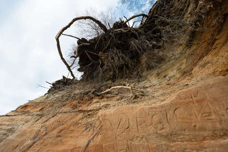 Limestone beach at the Baltic Sea with beautiful sand pattern and vivid red and orange color - Tourist writings on the walls and rocks and sand - Veczemju Klintis, Latvia - April 13, 2019の写真素材