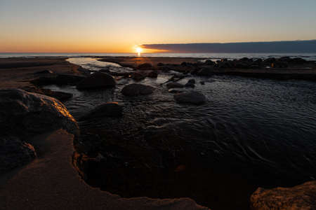 Beautiful sunset with red sand and spring water from a river exiting to the sea - Veczemju Klintis, Latvia - April 13, 2019の写真素材