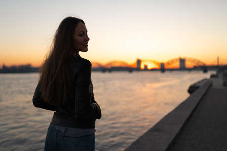 Young woman enjoying a sunset walk along the river Daugava with a view over clear blue skyの写真素材