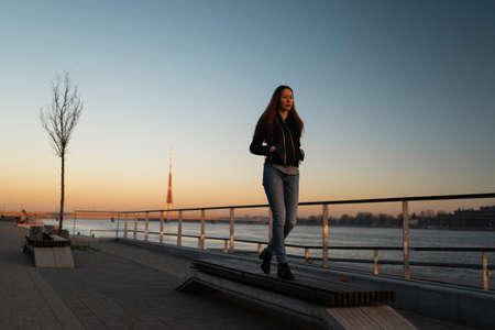 Young woman feeling confident during a lifestyle walk along the River Daugava at a sunsetの写真素材