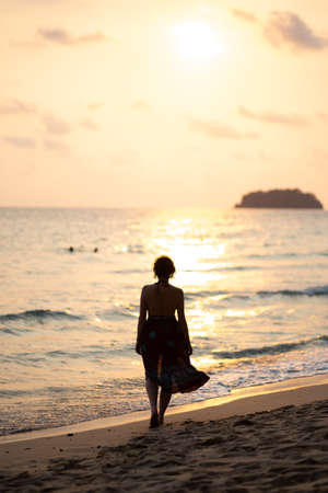 Beautiful woman in a colorful summer dress walking on the Thailand Ko Chang beach with beautiful white send during a sunsetの写真素材