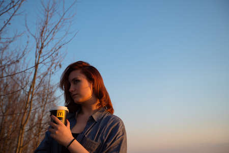 MARUPE, LATVIA - APRIL 22, 2019: Young woman drinking McDonalds coffee outdoors in a field during...