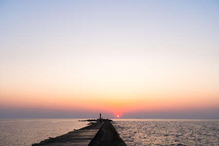 Lighthouse during a last minute of sunset with a big sun close to the horizon and clear skyの写真素材