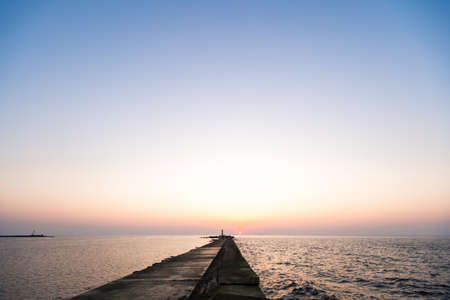 Lighthouse during a last minute of sunset with a big sun close to the horizon and clear skyの写真素材