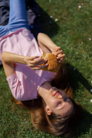 Successful business woman eating fast food burger cheesburger enjoys her leisure free time in a park...