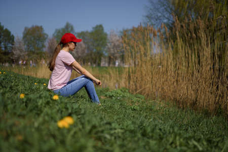 Successful business woman enjoys her leisure free time in a park with blossoming sakura cherry trees wearing jeans, pink t-shirt and a fashion red capの写真素材
