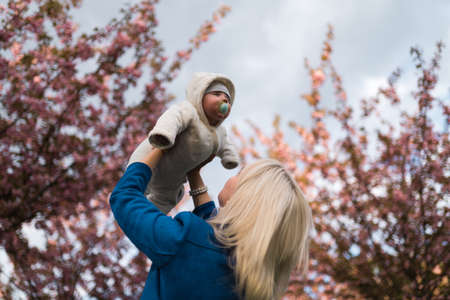 Young mother woman enjoying free time with her baby boy child - Caucasian white child with a parents hand visible - Dressed in white overall with hearts, mom in blueの写真素材