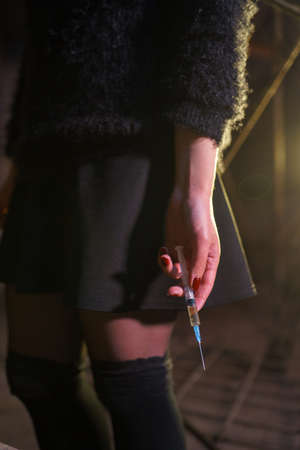 Syringe close up in hands of a drug addiction redhead caucasian white young woman wearing black sweater, skirt and chocker - Anxiety, depression and danger feelingの写真素材