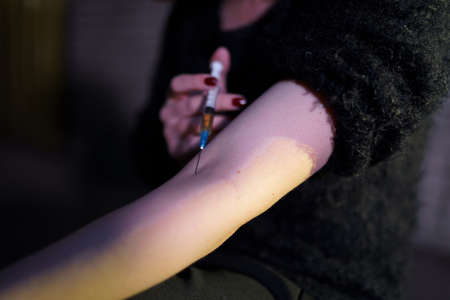 Veins syringe close up in hands of a drug addiction redhead caucasian white young woman wearing black sweater, skirt and chocker - Anxiety, depression and danger feelingの写真素材