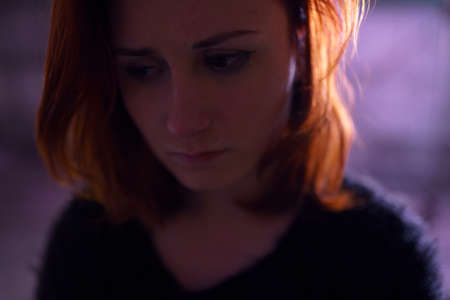 Face portrait close up of drug addiction redhead caucasian white young woman wearing black sweater, skirt and chocker with syringe and pills in the background - Anxiety, depression and danger feelingの写真素材