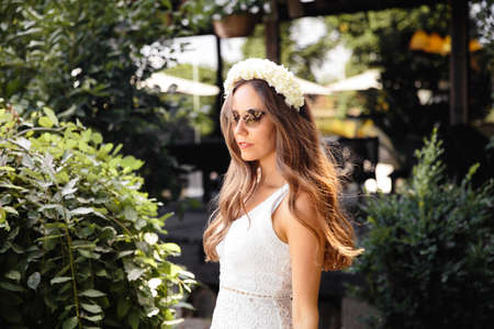 Beautiful woman in white portrait in an outdoor cafe garden in summer or early autumn with green grass and treesの写真素材
