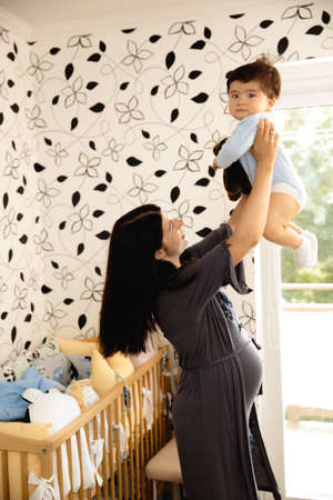 Pregnant Mother holding playing with her baby son talking with him - Asian mixed ethnicity child Boy...