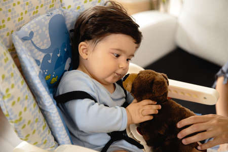 Mother feeding her baby son porridge in the child seat - Asian mixed ethnicity child Boy wearing...