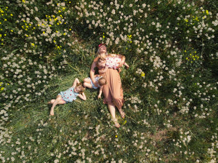 Aerial drone: Mother having quality funny playing time with her baby girls at a park blowing dandelion - Young blonde hippie - Daughters wear similar dresses with strawberry print - Family valuesの写真素材
