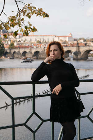 Happy redhead tourist traveler in Prague, Czech Republic wearing black sweater with Charles Bridge in the backgroundの写真素材
