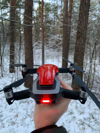 Man hand holding bright red drone to be lift up in a snow forest in Baltics Riga Latvia - Cold snow...